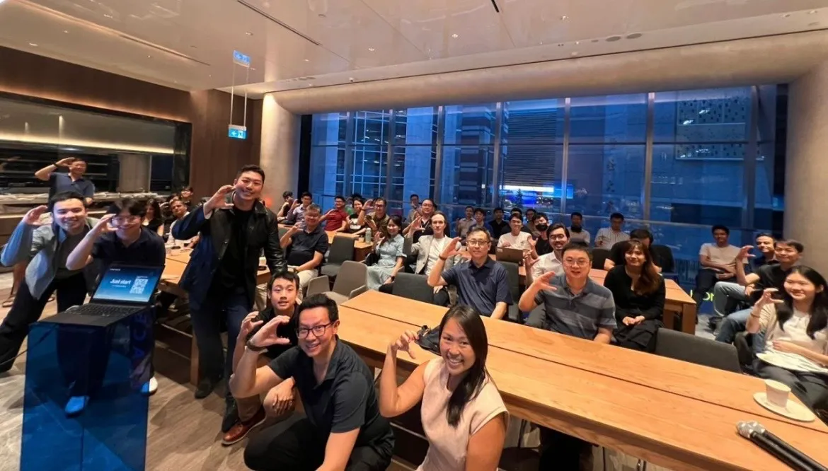 About forty people from an AI agent community group waving at the camera, in a room with floor-to-ceiling windows.