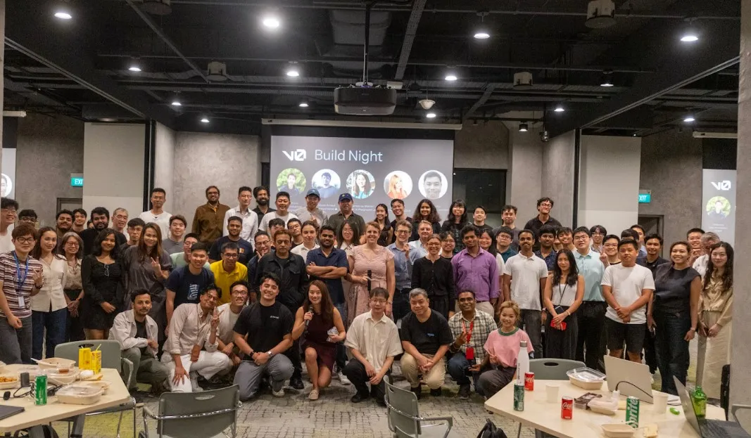 Group photo of around a hundred people at v0 Build Night, in front of a projected title slide.